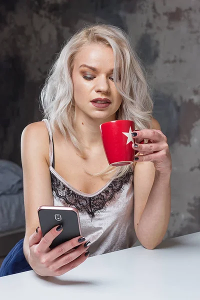 Krásná blondýnka v domácí oblečení používá smartphone — Stock fotografie