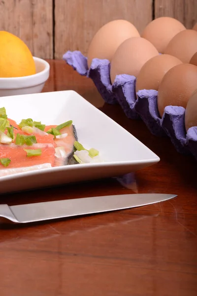 Filete de salmón fresco de cerca en el plato blanco. cuchillo, huevos y limón —  Fotos de Stock