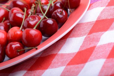 Sweet cherries in bowl on red and white material close up clipart