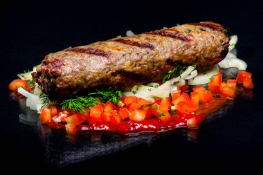 Lula kebab with vegetables and herbs on a black background.