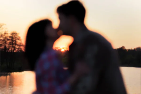 Couple kissing at the lake at sunset, blur