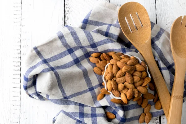 Nuts, almond, tasty and healthy food with lots of vitamins. Almond nuts on white wooden background with two wooden spoons and white towel with blue stripes