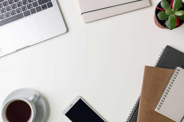 Top view of office workplace. White desk with copy space. Flat lay view on table with laptop, phone, notebooks, flower and cup of coffee. Creative designer concept.