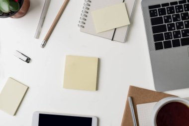 Üstten Görünüm office çalışma alanı'nın. Kopya alanı ile beyaz Masası. Düz yatıyordu görünümü dizüstü bilgisayar, telefon, dizüstü bilgisayarlar, fincan kahve, çiçek ve çıkartmalar, memopads tablo. Yaratıcı tasarımcı kavramı.