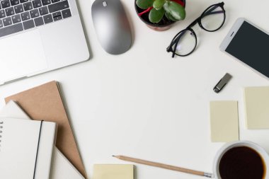 Üstten Görünüm office çalışma alanı'nın. Kopya alanı ile beyaz Masası. Dizüstü bilgisayar, telefon, flash sürücü, çiçek, defter, kalem, kahve, gözlük ve çıkartmaları veya faturası yastıkları masada düz yatıyordu görünümü.