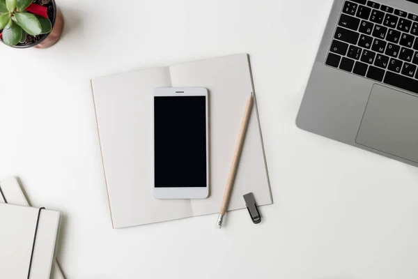 Üstten Görünüm office çalışma alanı'nın. Kopya alanı ile beyaz Masası. Dizüstü bilgisayar, telefon, çiçek, dizüstü bilgisayarlar ile yat görünümü tablo, flash sürücü ve kalem. Yaratıcı tasarımcı kavramı.