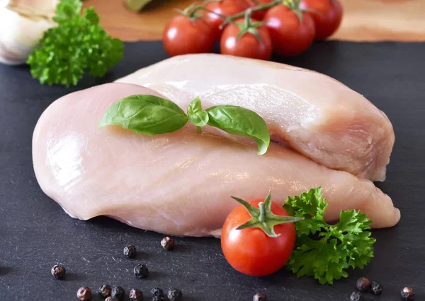 Pechuga de pollo cruda en un plato de pizarra, con tomates cherry frescos — Foto de Stock