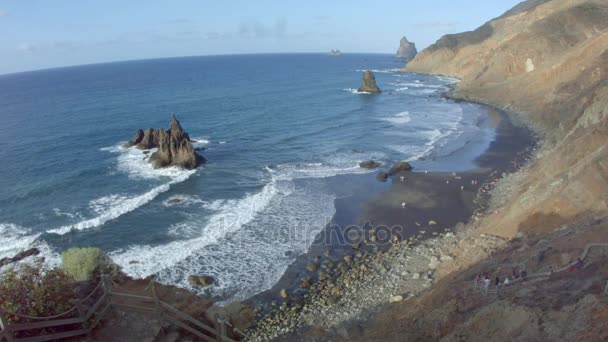 Vista desde lo alto de la playa de arena negra con ondulaciones y rocas en el mar — Vídeos de Stock