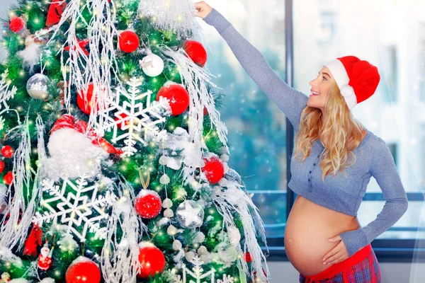 Pregnant woman adorns Christmas tree — Stock Photo, Image