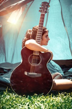 Yaz kampında tatil yapmaktan zevk alan genç bir kız, çadırın yanında gitar çalan güzel bir çocuk, şarkı söyleyen ve güneşli bir yaz zamanı eğlenen bir kız.