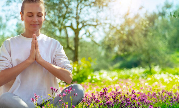 Женщина, занимающаяся йогой на свежем воздухе, симпатичная женщина в позе лотоса с закрытыми глазами в красивом цветущем весеннем саду, здоровый образ жизни, расслабление и оздоровительная концепция
