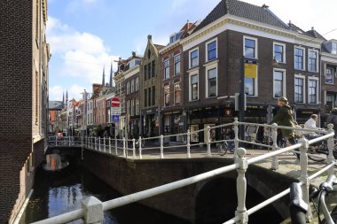 Delft, Hollanda - 10 Ekim 2019: Konut evleri ve kıyıya yakın bir su yolu manzarası, yürüyen ve bisiklet süren insanlar var.