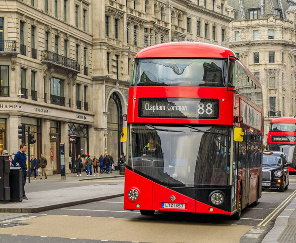 Luxury stores on Regent street with people passing and a double decker red buss on the road in London United Kingdom