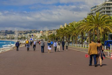 Nice, France - May 23, 2019: People on famous Promenade des Anglais with Mediterranean Sea coastline and Negresco hotel in the background, Cote d'Azur