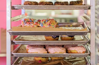 Fırıncıların yuvarlanan tava raflarında taze yapılmış donut seçimi popüler bir çörek zinciri dükkanında sergilenmeye hazır, seçici odaklı