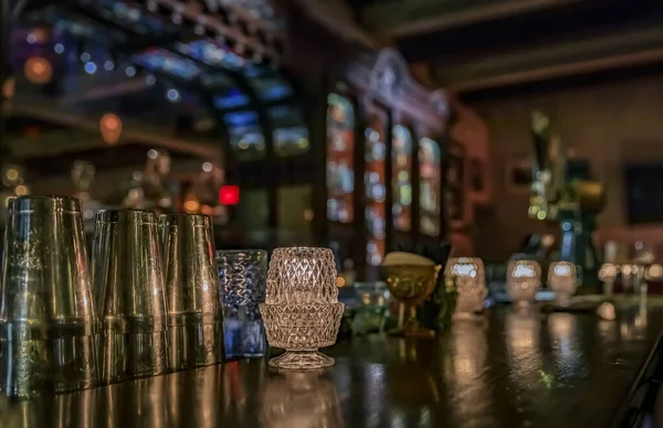 Старая деревянная стойка бара со свечами, барными инструментами и размытым барокко или викторианским баром с бутылками на заднем плане — стоковое фото