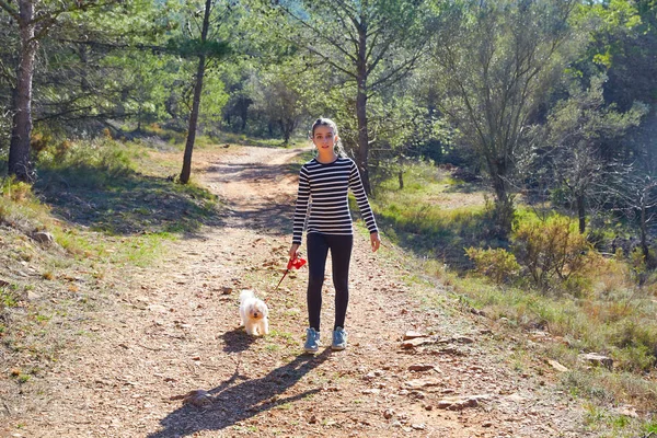 Teenie-Mädchen geht mit weißem Hund im Wald spazieren — Stockfoto