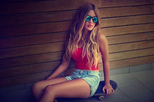 Blond teen dívka sedí na brusle v dřevěné stěně — Stock fotografie