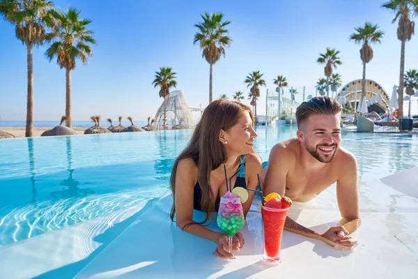 Pareja joven en infinito piscina cócteles — Foto de Stock