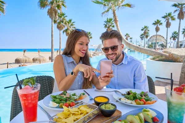 Pareja joven con smartphone en restaurante piscina — Foto de Stock