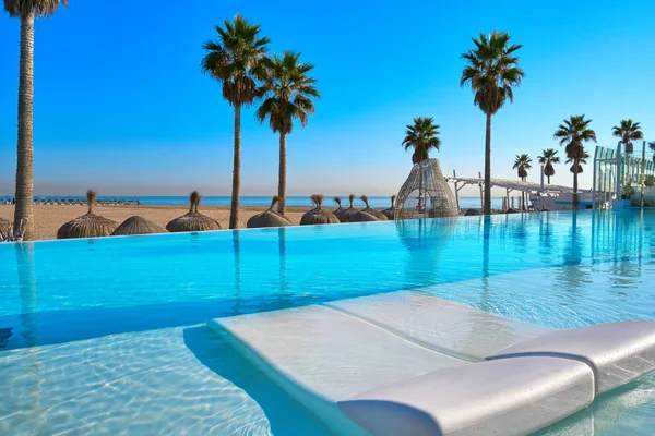 Resort piscina infinita en una playa con palmeras —  Fotos de Stock
