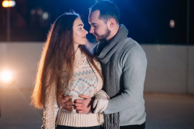 Romantik bir çift randevuda. Genç çift karlı kış manzarasında açık buz pateni pistinde birlikte duruyorlar.