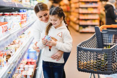 Süpermarkette bir aile. Güzel genç anne ve küçük kızı gülümseyip yiyecek alıyorlar. Sağlıklı beslenme kavramı. Hasat et