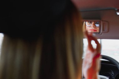 Bir arabanın dikiz aynasına bakan genç bir kadın.