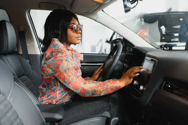 Woman buying the car. Lady in a car salon. Elegant black girl