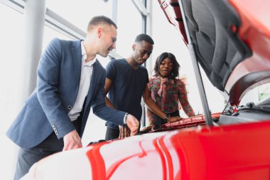 Mutlu Afrikalı araba satıcısı müşterilere araba motoru gösteriyor.