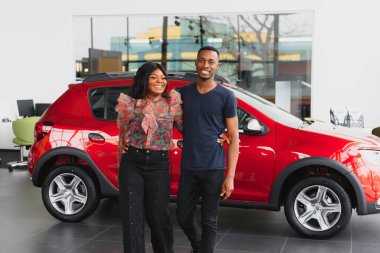 Gülümseyen Afrikalı Amerikalı çift yeni araba galerisinde kameraya sarılıp gülümsüyor.