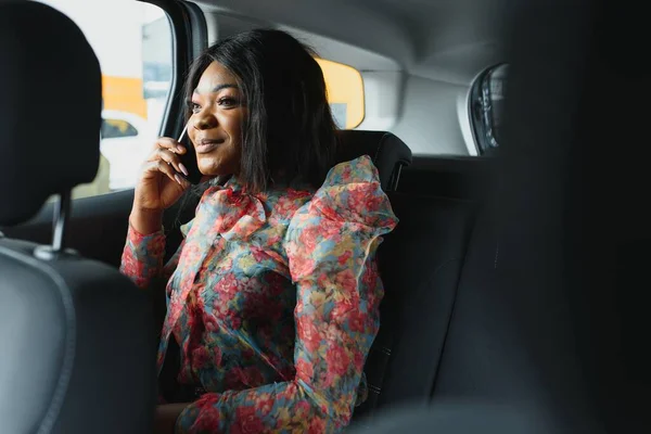 business trip, transportation, travel, gesture and people concept - young smiling african american woman calling on smartphone in car at city street