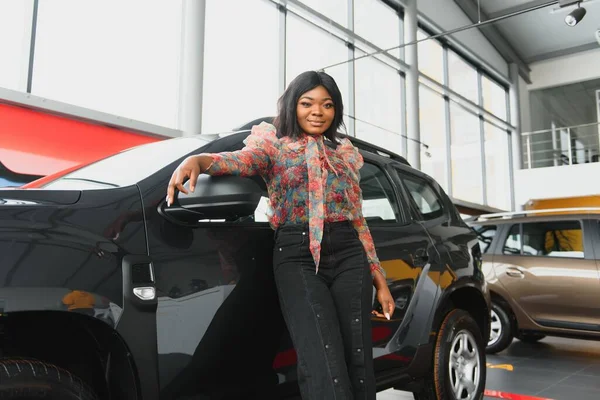 Woman buying the car. Lady in a car salon. Elegant black girl