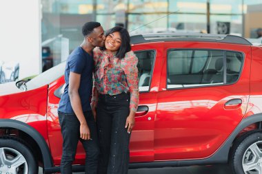 Gülümseyen Afrikalı Amerikalı çift yeni araba galerisinde kameraya sarılıp gülümsüyor.