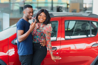 Gülümseyen Afrikalı Amerikalı çift yeni araba galerisinde kameraya sarılıp gülümsüyor.