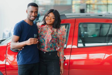 Gülümseyen Afrikalı Amerikalı çift yeni araba galerisinde kameraya sarılıp gülümsüyor.
