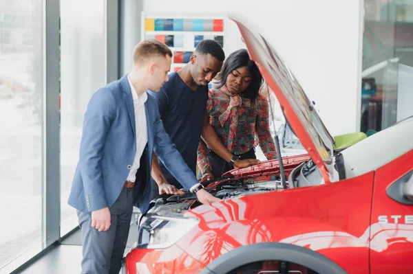 happy african car salesman showing car engine to customers