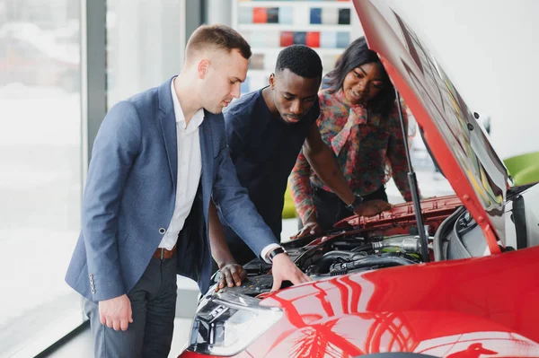 Mutlu Afrikalı araba satıcısı müşterilere araba motoru gösteriyor.