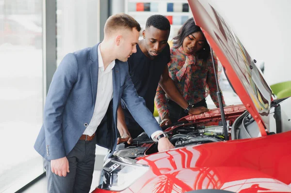 Mutlu Afrikalı araba satıcısı müşterilere araba motoru gösteriyor.