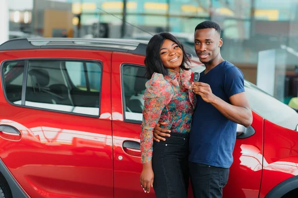 Gülümseyen Afrikalı Amerikalı çift yeni araba galerisinde kameraya sarılıp gülümsüyor.