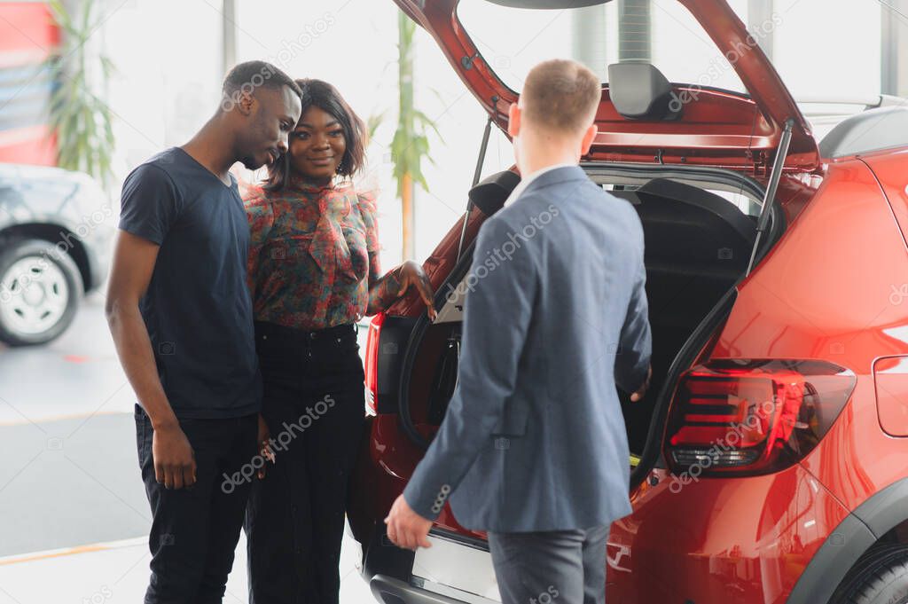 salesman showing new car to african couple in showroom