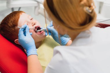 Maske takan bir dişçi. Kızıl saçlı, maske takan çocuk dişçisi yakışıklı çocuğu muayene ediyor.