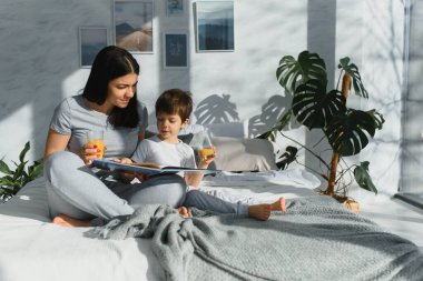 Sabahları oğluyla birlikte yatakta meyve suyu içen güzel bir kadın. Sağlıklı yeme kavramı