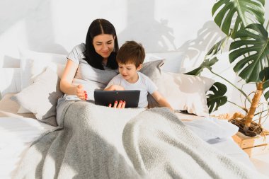 Güzel, gülümseyen anne ve oğul yatakta dijital tabletle oynuyorlar..
