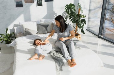 Genç bir anne ve 5 yaşındaki küçük oğlu pijama giyip hafta sonu birlikte yatakta oynuyorlar. Tembel bir sabah, sıcak ve rahat bir ortam. Aile evi çekimi.