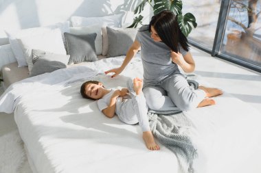 Genç bir anne ve 5 yaşındaki küçük oğlu pijama giyip hafta sonu birlikte yatakta oynuyorlar. Tembel bir sabah, sıcak ve rahat bir ortam. Aile evi çekimi.