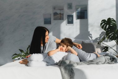 Genç anne ve 4 yaşındaki oğlu pijama giyip hafta sonu yatakta oynuyorlar. Tembel sabah, sıcak ve rahat bir ortam..