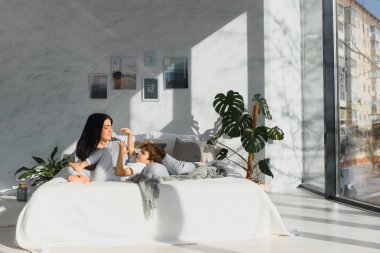 Genç anne ve 4 yaşındaki oğlu pijama giyip hafta sonu yatakta oynuyorlar. Tembel sabah, sıcak ve rahat bir ortam..