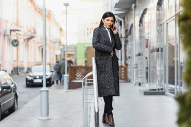 Şehirdeki çekici genç kadın. İş kadını, modern iş merkezinin önünde akıllı bir telefonla konuşurken gülümsüyor.