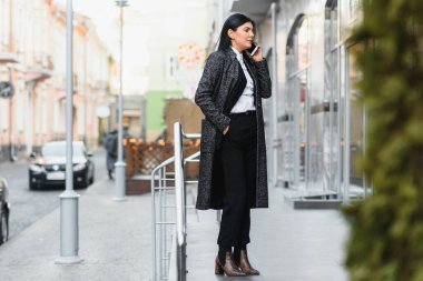 Şehirdeki çekici genç kadın. İş kadını, modern iş merkezinin önünde akıllı bir telefonla konuşurken gülümsüyor.